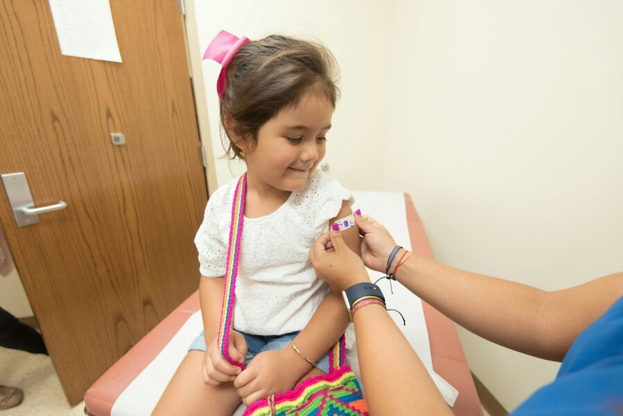 Little smiling girl sits while a nurse applies a bandage to her left arm